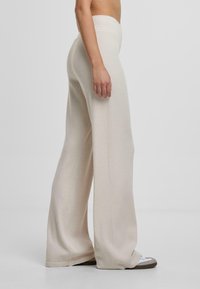 Pantalons larges en tricot beige avec une taille haute, texture lisse et silhouette fluide, associés à des chaussures confortables.