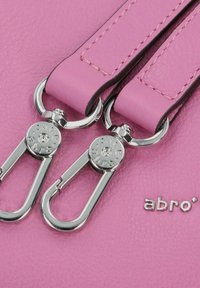 Dettaglio di una borsa in pelle rosa con hardware metallico e distintivi ganci di chiusura. Include cuciture pronunciate e logo del marchio in rilievo.