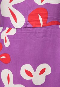 Μωβ ύφασμα με φυτικό μοτίβο που περιλαμβάνει μεγάλα λευκά και κόκκινα λουλούδια. Η υφή φαίνεται λεία με ελαφριά γυαλάδα.