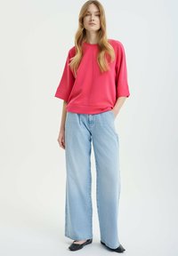 Pink oversized sweatshirt with dropped shoulders, paired with light blue wide-leg denim jeans and black flat shoes.