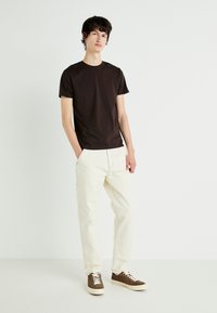 Brown cotton t-shirt paired with cream cargo pants. Model wears brown and white sneakers. The background is plain white for contrast.