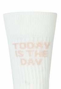 Calzino bianco a coste con il testo "Oggi è il giorno" in un delicato colore pesca. Il materiale è lavorato a maglia, offrendo un aspetto testurizzato.