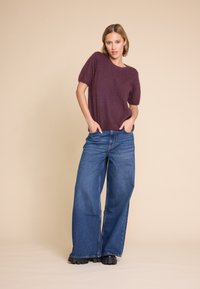 Burgunderfarget genser med kort erme laget av mykt materiale, kombineres med vide blå denimjeans. Antrekket har avslappet passform og klassisk denimtekstur.