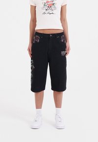 Pantalones cortos de mezclilla negros con bolsillos de patrón floral, bordado gráfico en el lado izquierdo y un corte relajado que llega por debajo de la rodilla.