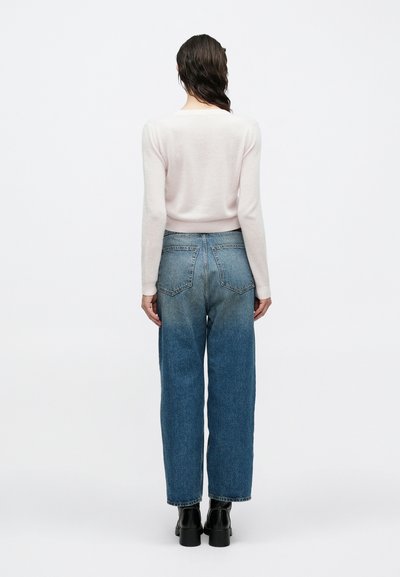 Világos rózsaszín kötött pulóver hosszú ujjal, magas derekú, koptatott hatású, egyenes szárú kék farmernadrággal párosítva. Fekete bokacsizma.