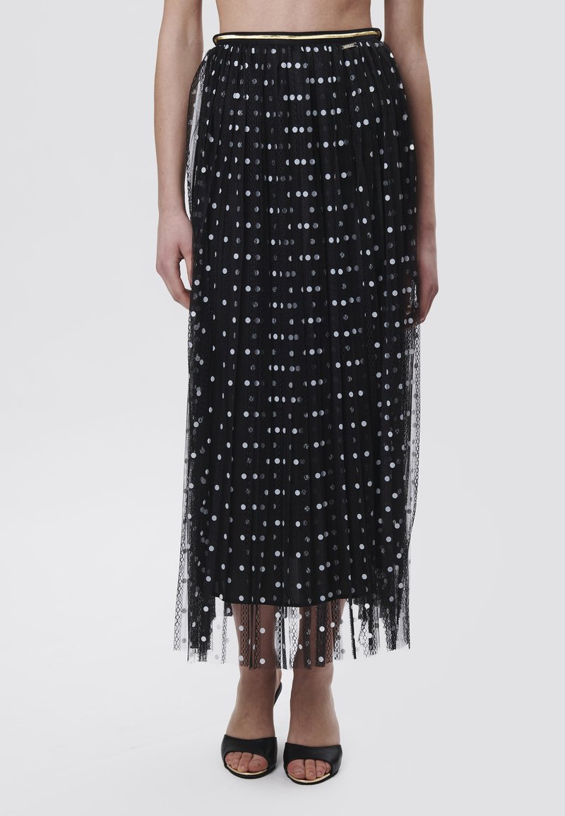 Jupe en tulle noire avec des pois argentés, design plissé, taille élastique avec garniture dorée, longueur cheville, paire de talons ouverts noirs.