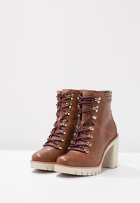 Bottes chelsea en cuir marron avec des lacets violets, des finitions dorées, un talon épais crème et une semelle robuste. Finition texturée et détail de col rembourré.
