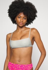 Top de bikini cinza texturizado com formato quadrado e alças finas, combinado com um fundo rosa brilhante apresentando um padrão de estampa de leopardo.