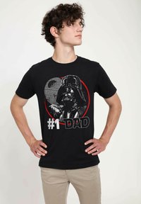 Černé bavlněné tričko s grafikou postavy v přilbě, textem "DAD" a designem kruhu se detailem vesmírného pozadí.