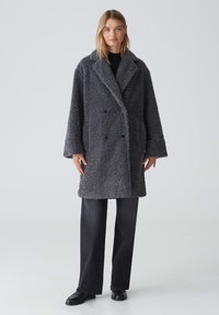 Gray, oversized double-breasted coat made of fuzzy fabric with a textured surface, featuring large lapels and front buttons.