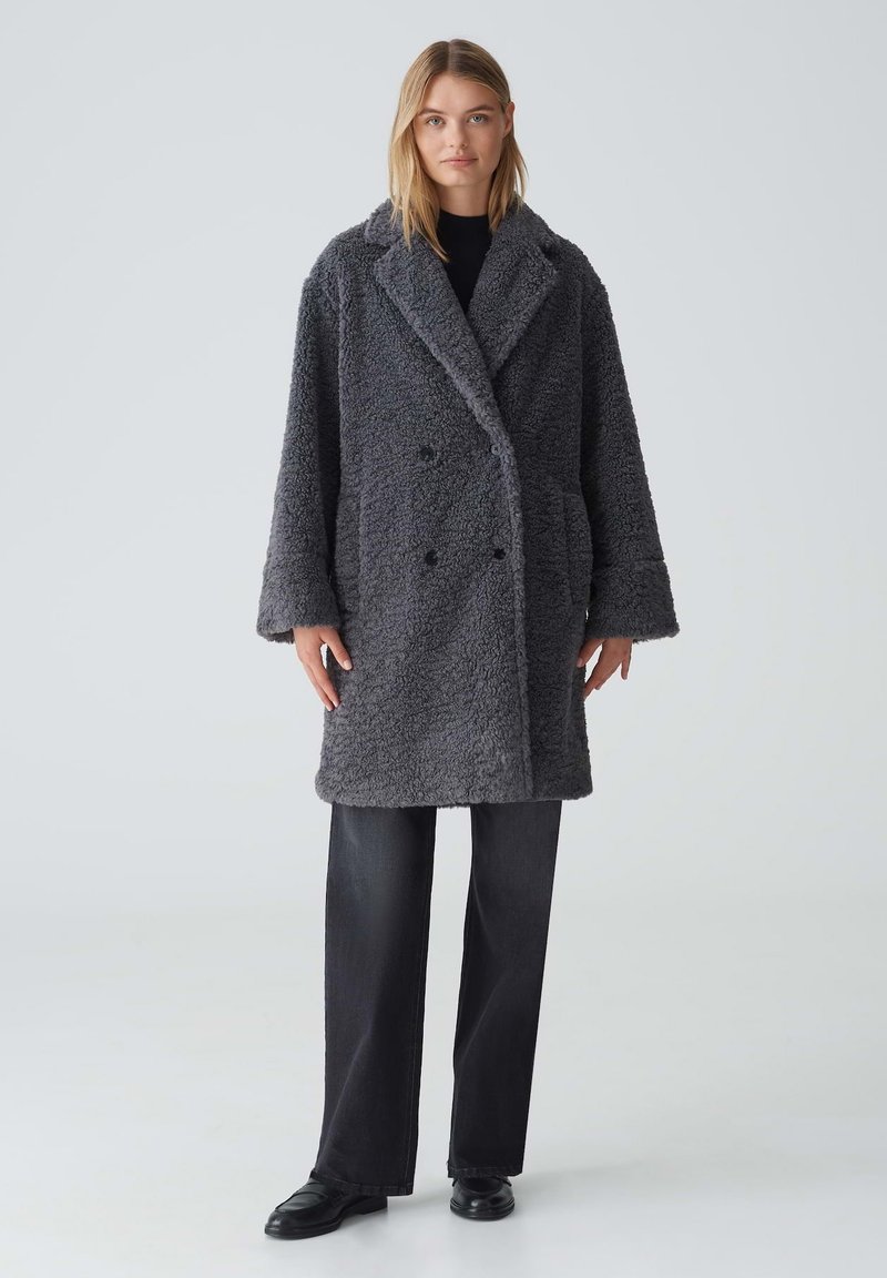 Gray, oversized double-breasted coat made of fuzzy fabric with a textured surface, featuring large lapels and front buttons.