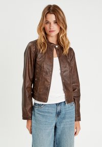 Bruine leren jas met een getailleerd ontwerp, ritsluiting en drukknoopkraag. Voorzien van zijzakken en een zachte textuur. Gecombineerd met lichte jeans.