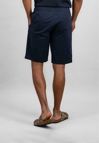 Navy blue shorts with an elastic waistband, side and back pockets. Worn with brown slide sandals, showcasing a smooth texture and casual design.