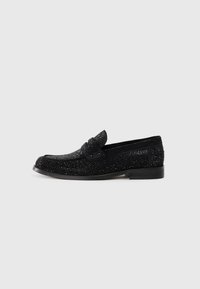 Svart herrskor i loafermodell med glittrande detaljer, låg klack och en pennyrem, visade i profil mot en enfärgad bakgrund.