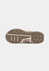 Semelle de chaussure de sport avec une texture en caoutchouc marron, présentant des motifs de grip rectangulaires et circulaires, et une bande blanche sur le côté.