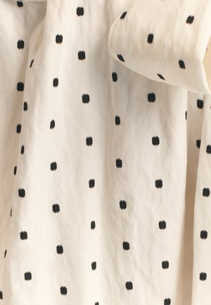 Bomuldsstof med en cremefarvet baggrund og små, jævnt fordelte sorte prikkede firkanter, der skaber en enkel, mønstret tekstur.