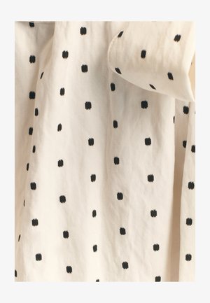 Tkanina bawełniana z kremowym tłem i małymi, równomiernie rozmieszczonymi czarnymi kropkowymi kwadratami, tworzącymi prostą, wzorzystą teksturę.