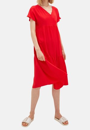 Czerwona sukienka do kolan z dekoltem w serek, krótkimi rękawami i falbanami na dole. Gładka tkanina o luźnym kroju. Połączona z białymi sandałami wsuwanymi.