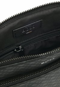 Pouch in tessuto nero con motivo testurizzato, chiusura zip e tasca interna. Presenta un'etichetta impressa con la scritta "BOSS". Finitura liscia e opaca.