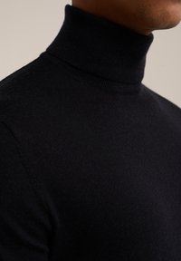 Pull à col roulé noir en tissu tricoté doux, avec une coupe ajustée et un col côtelé, présentant une texture lisse.