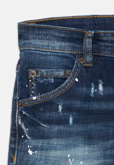 Tummansiniset farkut, joissa kulutettuja kohtia ja valkoisia maalitahroja. Mukana perinteiset taskut ja kontrastiväriset ompeleet.