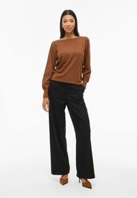 Pull en maille marron avec un col bateau, associé à un pantalon noir à jambes larges. La tenue présente une texture subtile et des manches ajustées.
