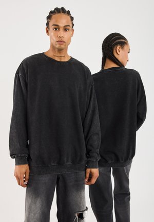 Svart oversized sweatshirt med en slitt finish, med ribbestrikkede mansjetter og kant, samt rund hals. Kombinert med falmede svarte jeans.
