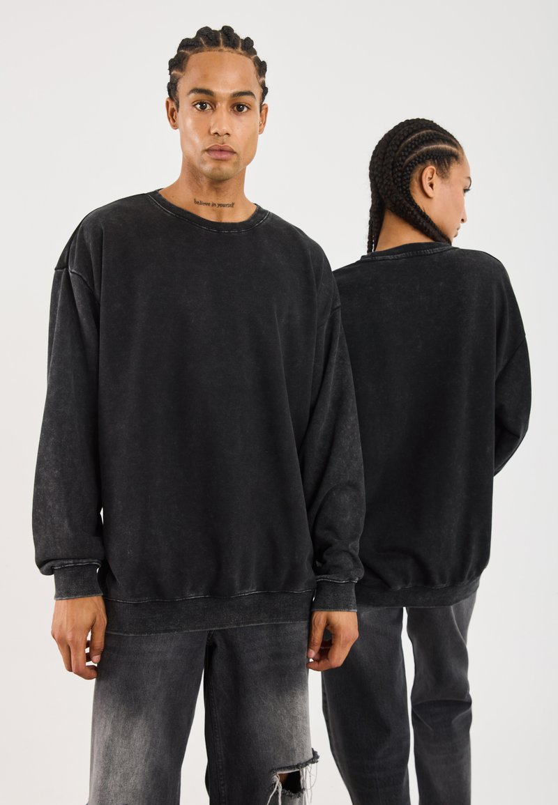 Svart oversized sweatshirt med en slitt finish, med ribbestrikkede mansjetter og kant, samt rund hals. Kombinert med falmede svarte jeans.