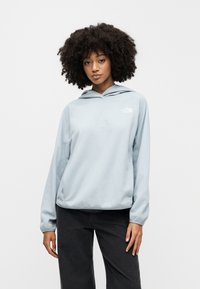 Φούτερ με ελαφρώς γαλάζιο fleece, κουκούλα με κορδόνι, άνετη εφαρμογή και λευκό λογότυπο στο αριστερό στήθος. Συνδυασμένο με σκούρο, φαρδύ παντελόνι.