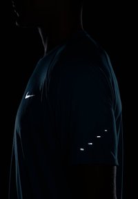 T-shirt desportivo da Nike, azul escuro, com um logótipo refletor no peito e detalhes refletivos na manga. Tecido macio e respirável.
