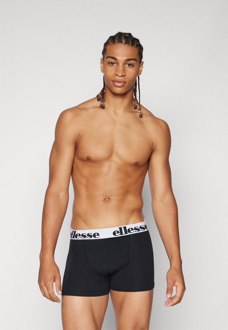 Svarta boxershorts med en vit "ellesse" logoband, med en mjuk textur och en figurnära design. Modellen har flätat hår.