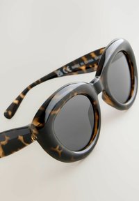 Gafas de sol carey con montura redondeada, acabado brillante y lentes oscuros. Patrón notable de acentos marrones y negros en las patillas.