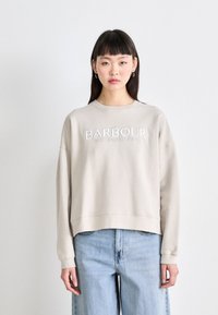 Beige színű pulóver kerek nyakkal, hímzett "BARBOUR INTERNATIONAL" logóval és laza fazonnal. Világoskék, laza szabású farmerral párosítva.