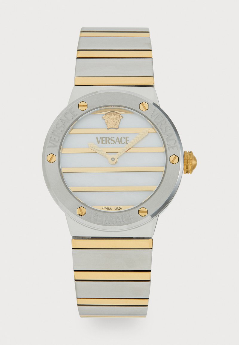Versace pulkstenis ar apaļu sudraba korpusu, zelta akcentu svītrām, baltu svītru ciparnīcu un logotipa detaļām; nerūsējošā tērauda siksna ar mainīgām zelta svītrām.