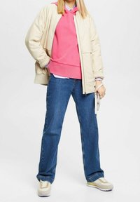 Beige quiltad jacka, rosa hoodie, blå vida jeans och beige sneakers. Funktioner inkluderar lagerkläder och en minimalistisk handväska.