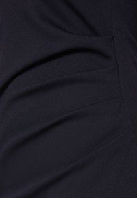 Melnā, faktūrētā auduma ar smalkām krokām. Dizains ietver mīkstus salocījumus un vīles, izceļot gludu, plūstošu siluetu.