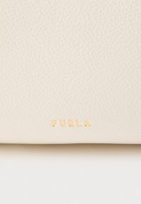 Bela teksturirana usnjena dodatna oprema z zlato vtisnjenim logotipom "FURLA". Gladek površinski z rahlim vzorcem zrnja, pravokotne oblike.