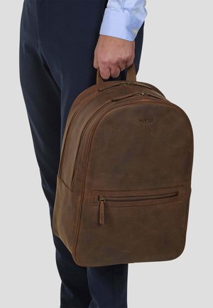 Brown leather backpack with rounded shape, two zippered compartments, front pocket with zipper, and sturdy top handle.