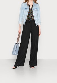 Jeansjacka, svart blommig blus, svarta vida byxor och svarta pumps med öppen tå. Ljusblå handväska med en texturerad rem.