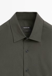 Dunkelgrünes Hemd mit klassischem Kragen, strukturiertem Stoff, zwei schwarzen Knöpfen und einem Etikett mit der Aufschrift "Massimo Dutti." Hergestellt in der Türkei.