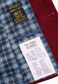 Maroon suit with a blue plaid lining featuring tags. Includes a care label with dining utensil illustrations and text instructions.