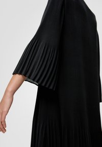 Svart ribbad klänning med korta veckade ärmar och en flödande silhuett. Tyget har en mjuk struktur med en subtil lyster.