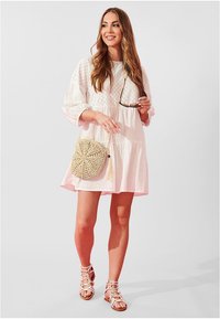 Witte jurk tot op de knie met gestructureerde details en pofmouwen. Geweven cirkelvormige handtas en lichtroze sandaaltjes met bandjes.