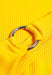 Tissu jaune côtelé avec un détail d'anneau métallique argenté. La texture est lisse, avec des coutures visibles le long des bords.