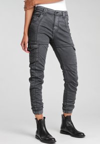 Pantalones cargo grises de corte ajustado, con múltiples bolsillos, una textura suave y puños elásticos, combinados con botas negras hasta el tobillo.