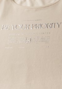 Beige bavlněné tričko s kulatým výstřihem a stříbrným potiskem s textem "BUĎTE SVOU PRIORITOU" a dalšími motivačními frázemi.