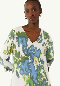V-Ausschnitt-Bluse aus leichtem Stoff mit einem lebhaften blauen und grünen abstrakten Muster, ausgestattet mit langen Ärmeln und einem lockeren Schnitt.