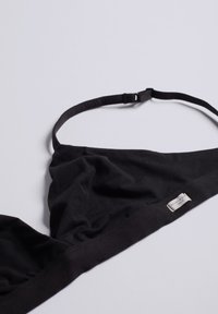 Svart bralette tillverkad av mjukt tyg, med triangulär form, tunna justerbara band och ett etikett på bandet.