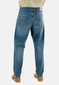 Jeans de denim azul con un corte holgado, que presentan un diseño clásico de cinco bolsillos. Los bolsillos traseros son diagonales y tienen un parche de cuero en la cintura.