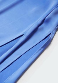 Helles blaues Gewebe mit glatter Textur, das seitliche Schlitze aufweist. Das Material erscheint dehnbar und weich, mit sauberen, verarbeiteten Kanten.
